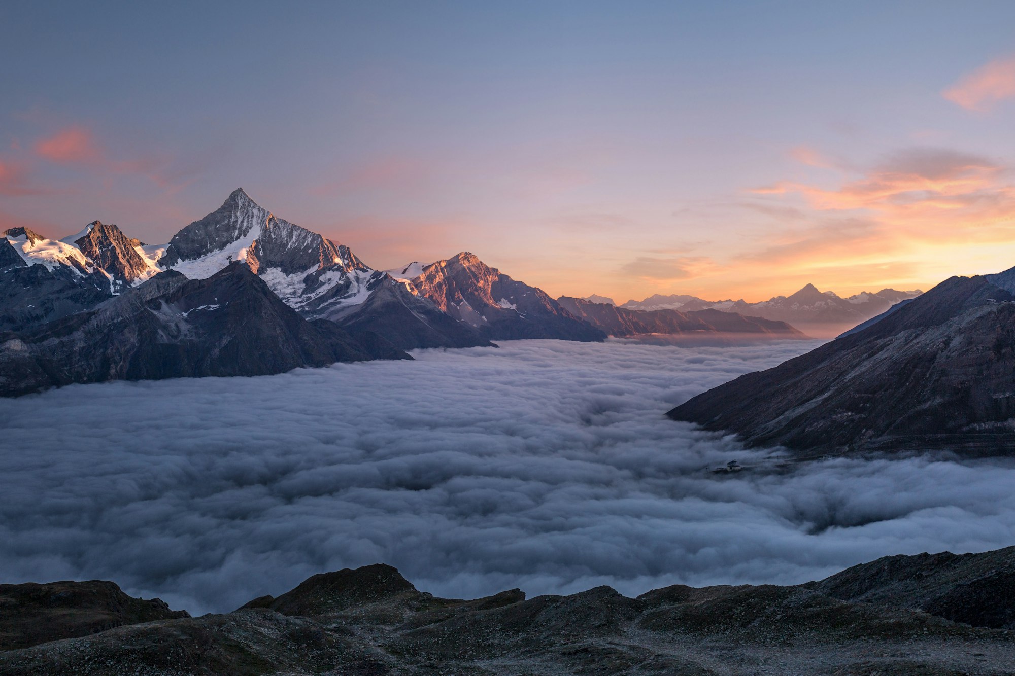 Snowy peaks rising above a sea of clouds at dusk