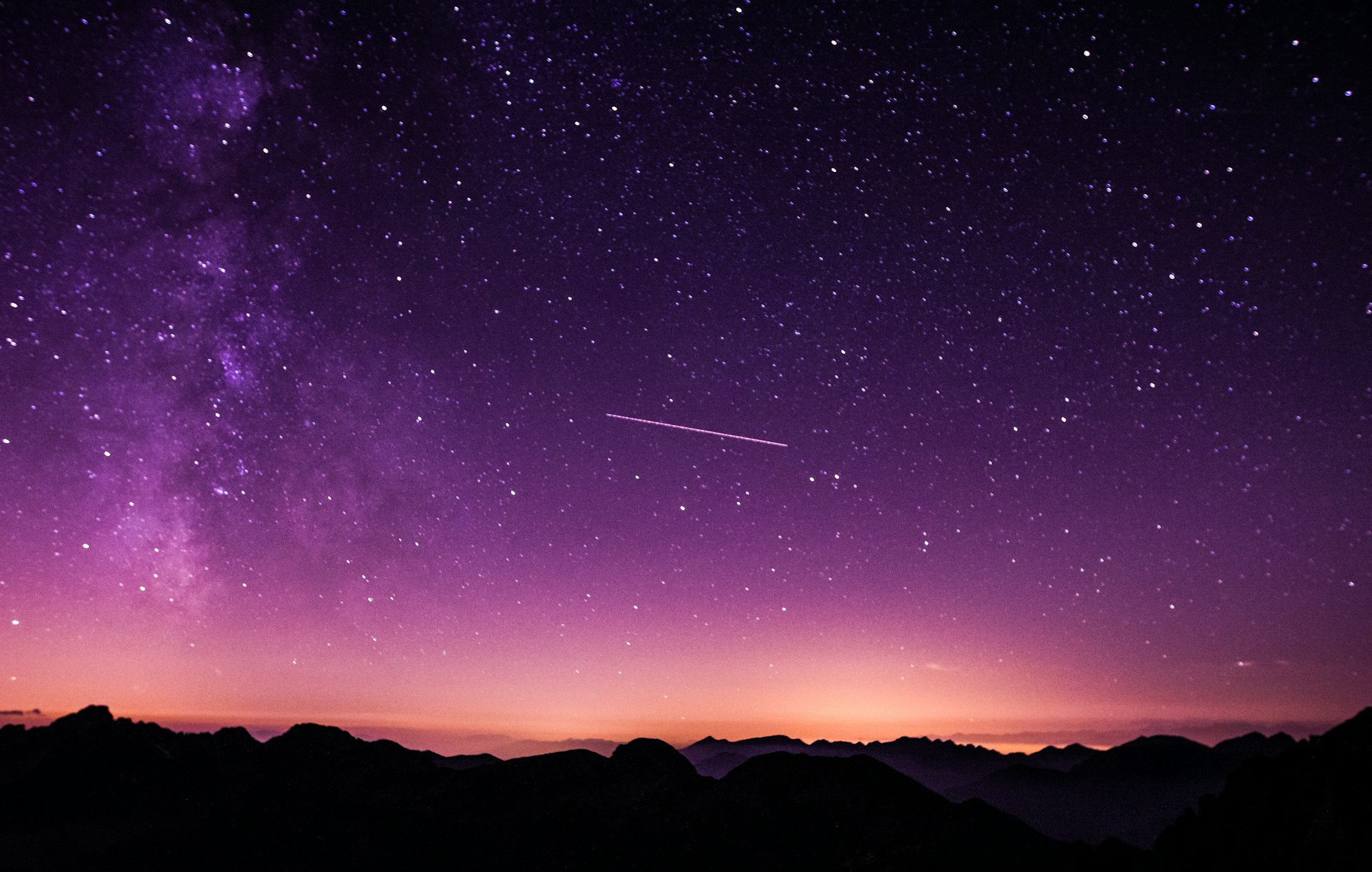 A violet night sky full of stars over a dark horizon